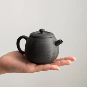 Handcrafted black Jingdezhen volcanic rock clay teapot held in palm showing compact size