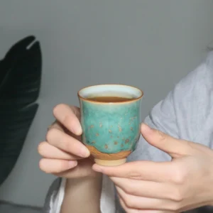 Handcrafted sea green porcelain tea cup with golden speckles and carved cloud base, side profile