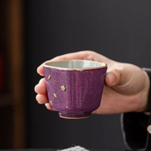 hand holding vintage chinese purple glaze porcelain nailed tea cup with gold floral detailing